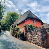 A cottage, rendered orange with a thatched roof, in front of which is a dry stone wall. Photo Credit: Agnieszka Mordaunt
