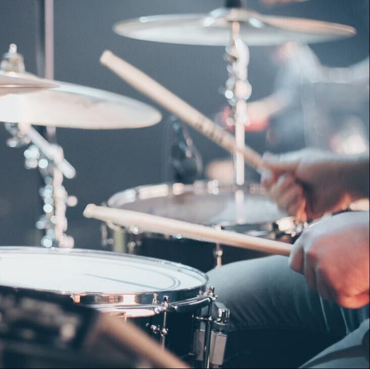 A brightly lit photo of someone playing a drum-set. Photo Credit: Josh Sorenson on Unsplash